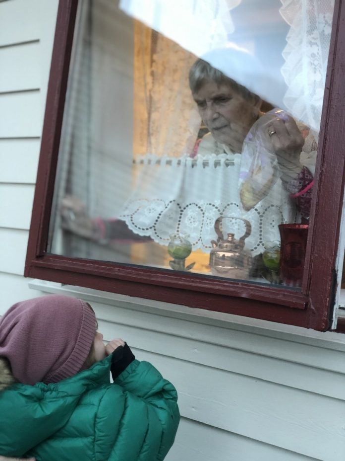 En gammel dame inne bak et vindu som er litt åpent, hvor hun snakker med et barn som står utenfor vinduet